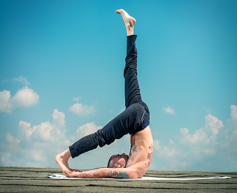 Yoga concept. Experienced yoga master performs various yoga poses on a roof over blue sky.